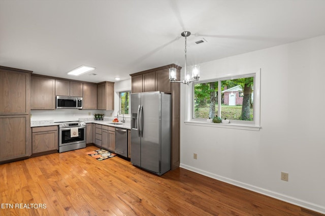 kitchen featuring sink, hanging light fixtures, stainless steel appliances, and light wood-type flooring