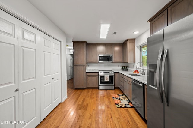 kitchen with dark brown cabinetry, sink, light hardwood / wood-style floors, and appliances with stainless steel finishes