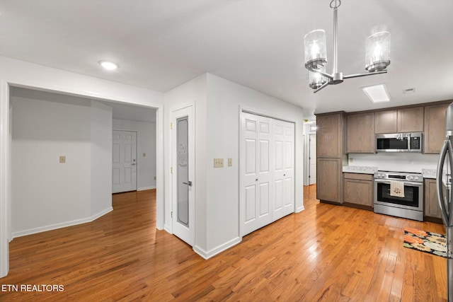 kitchen featuring a chandelier, appliances with stainless steel finishes, light wood-type flooring, and pendant lighting