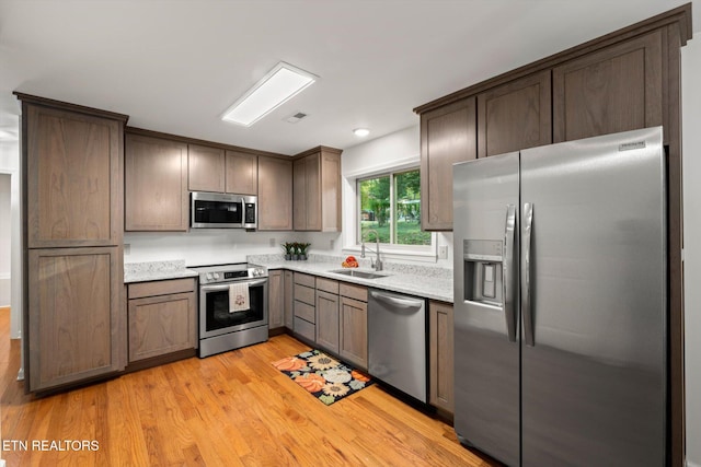 kitchen featuring appliances with stainless steel finishes, light hardwood / wood-style flooring, dark brown cabinets, and sink