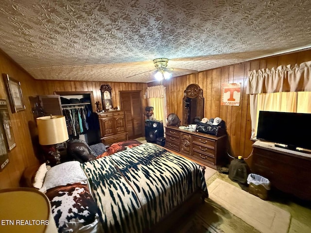 bedroom with a closet, a textured ceiling, wood walls, and a ceiling fan