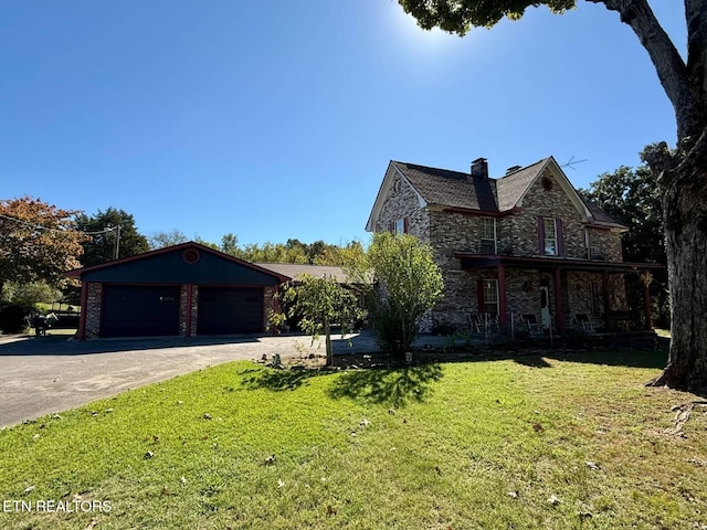 view of front facade featuring a front yard, a chimney, a garage, stone siding, and driveway