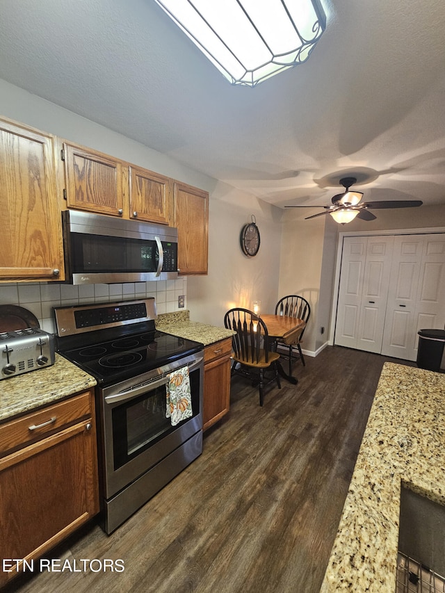 kitchen featuring dark wood-type flooring, backsplash, appliances with stainless steel finishes, light stone counters, and ceiling fan