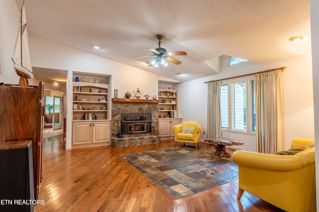 sitting room with lofted ceiling, ceiling fan, a textured ceiling, hardwood / wood-style flooring, and a wood stove