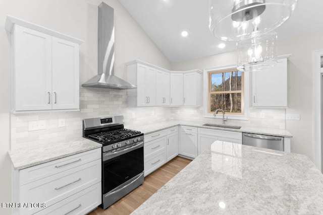 kitchen with pendant lighting, wall chimney range hood, sink, white cabinetry, and stainless steel appliances