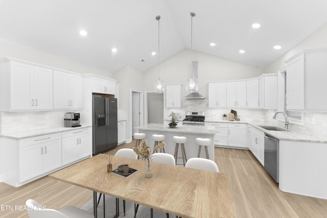 kitchen featuring wall chimney exhaust hood, appliances with stainless steel finishes, a kitchen island, pendant lighting, and white cabinets