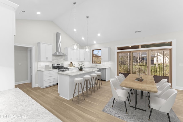 kitchen with stainless steel gas range oven, a kitchen island, pendant lighting, wall chimney range hood, and white cabinets