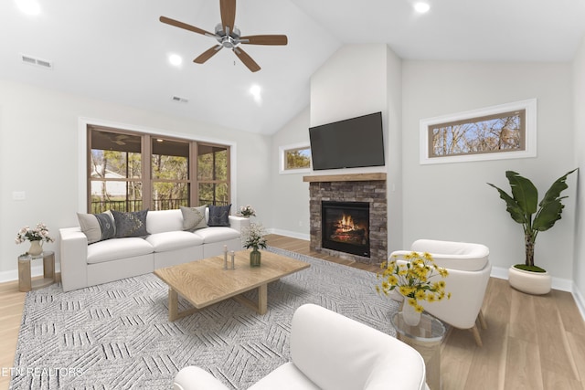 living room featuring ceiling fan, a stone fireplace, high vaulted ceiling, and light hardwood / wood-style floors