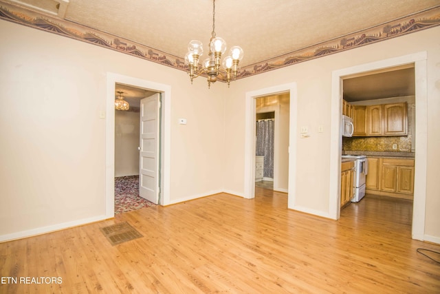 unfurnished dining area featuring an inviting chandelier, baseboards, light wood finished floors, and visible vents