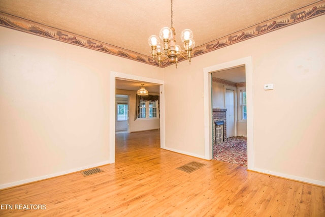 empty room with a textured ceiling, hardwood / wood-style flooring, and a chandelier