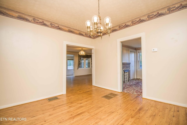 spare room featuring baseboards, a notable chandelier, light wood-style flooring, and visible vents