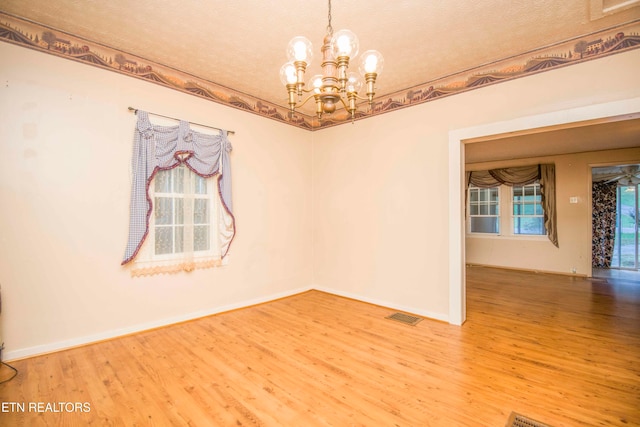 unfurnished room featuring a textured ceiling, hardwood / wood-style flooring, and an inviting chandelier