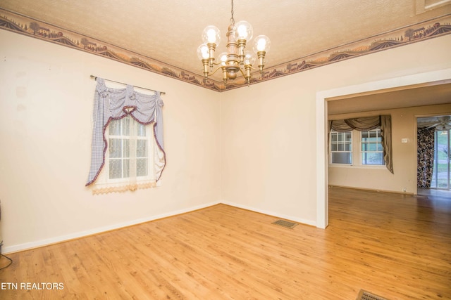 spare room featuring an inviting chandelier, a textured ceiling, baseboards, and wood finished floors
