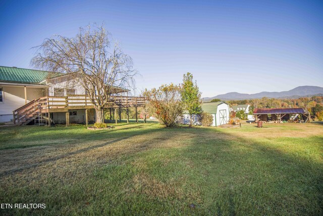 view of yard with a storage unit, a deck with mountain view, an outbuilding, and stairway