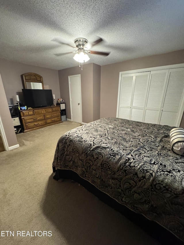 bedroom featuring a closet, a textured ceiling, light colored carpet, and ceiling fan