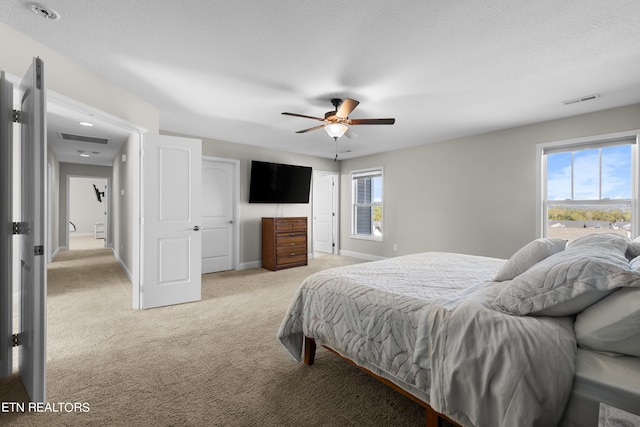 bedroom featuring light carpet, multiple windows, a textured ceiling, and ceiling fan