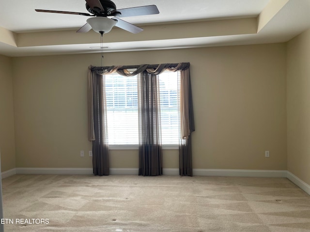 empty room with light carpet, a tray ceiling, and ceiling fan