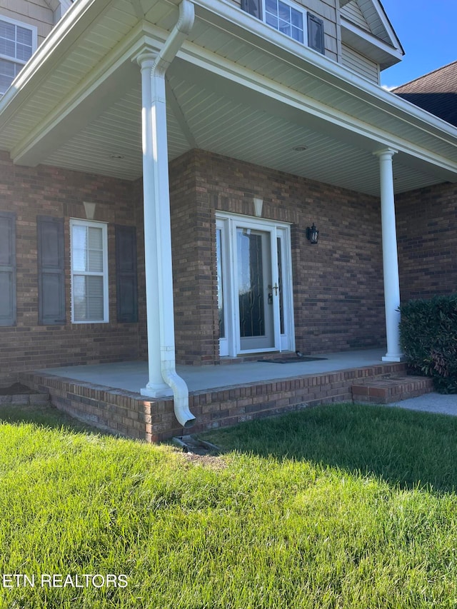 doorway to property featuring a porch and a lawn