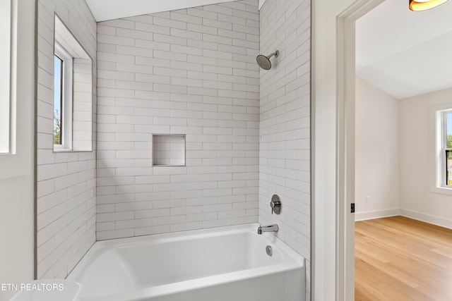 bathroom featuring tiled shower / bath combo, wood-type flooring, and vaulted ceiling