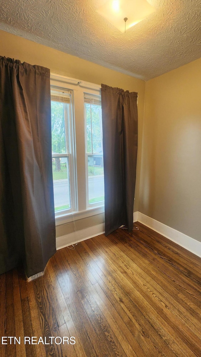 spare room with a textured ceiling and dark hardwood / wood-style flooring