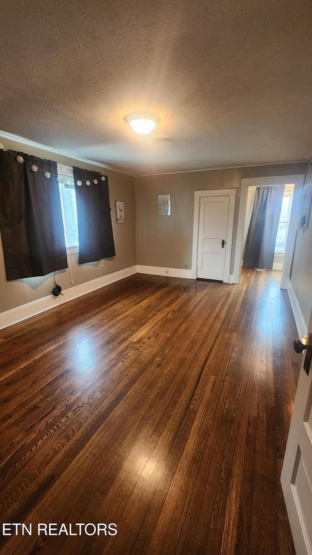 empty room featuring dark wood-type flooring, a textured ceiling, and a healthy amount of sunlight