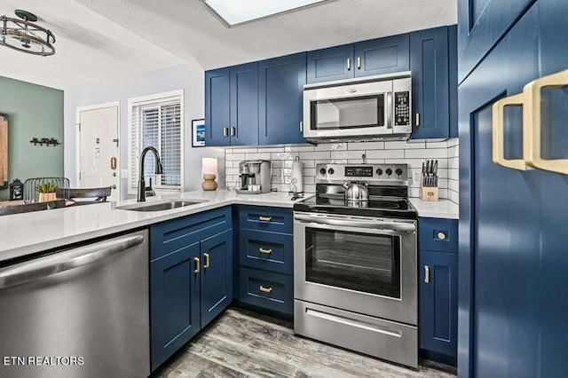 kitchen featuring light hardwood / wood-style flooring, backsplash, sink, blue cabinetry, and appliances with stainless steel finishes