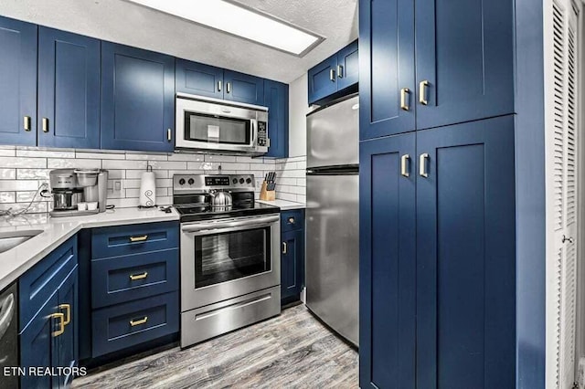 kitchen with blue cabinetry, appliances with stainless steel finishes, a textured ceiling, light hardwood / wood-style floors, and tasteful backsplash