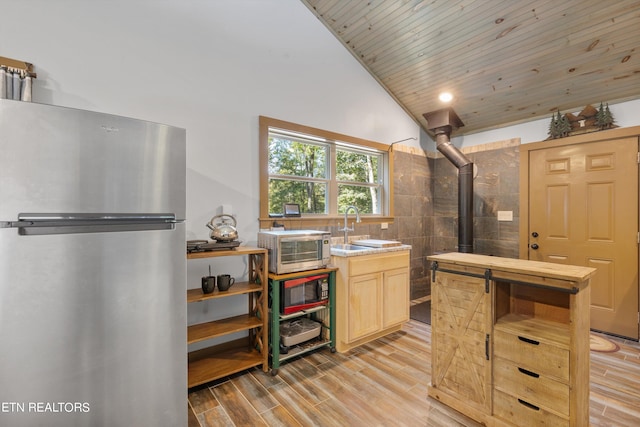 kitchen with light brown cabinets, appliances with stainless steel finishes, wooden ceiling, light hardwood / wood-style flooring, and a wood stove