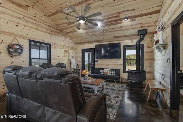 living room featuring wood ceiling, a wood stove, wooden walls, concrete flooring, and ceiling fan