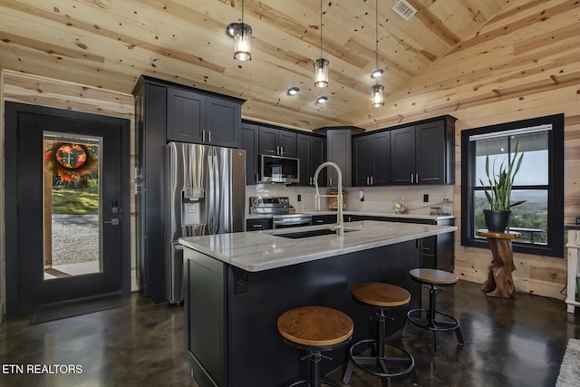 kitchen with light stone counters, appliances with stainless steel finishes, high vaulted ceiling, hanging light fixtures, and an island with sink