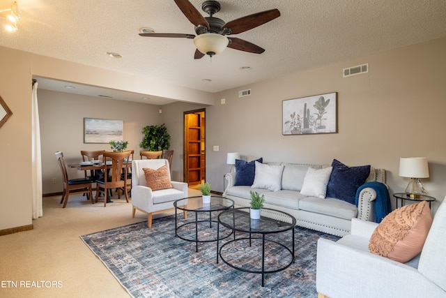 living room with ceiling fan, carpet flooring, and a textured ceiling