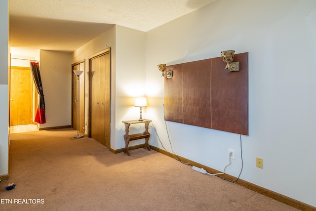 hall with a textured ceiling and light colored carpet