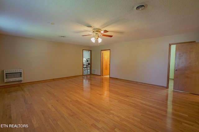 unfurnished room featuring a textured ceiling, light wood finished floors, visible vents, heating unit, and a ceiling fan