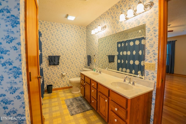 full bathroom with wallpapered walls, a sink, baseboards, and a textured ceiling