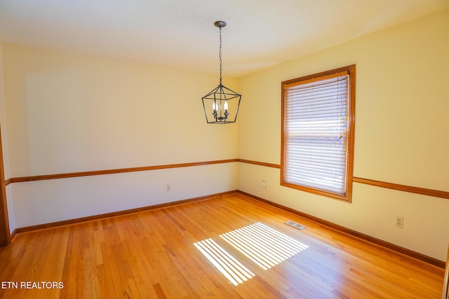 spare room with an inviting chandelier, light wood-style flooring, baseboards, and visible vents