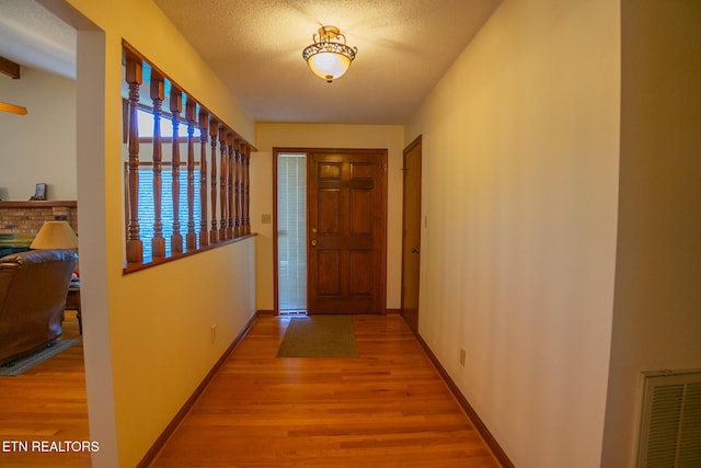 corridor featuring visible vents, a textured ceiling, baseboards, and wood finished floors