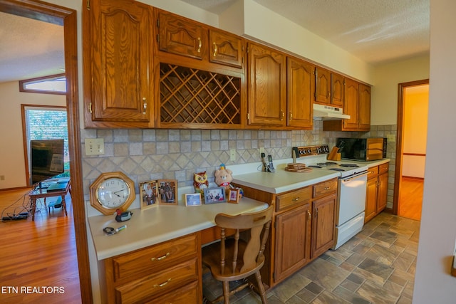 kitchen with light countertops, under cabinet range hood, electric stove, built in study area, and brown cabinetry