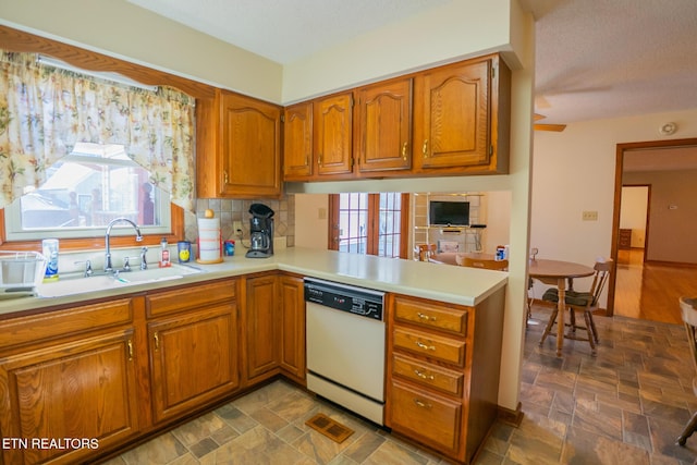 kitchen featuring decorative backsplash, light countertops, a sink, white dishwasher, and brown cabinetry