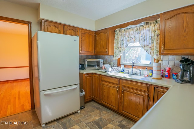 kitchen with light countertops, brown cabinets, tasteful backsplash, a sink, and freestanding refrigerator