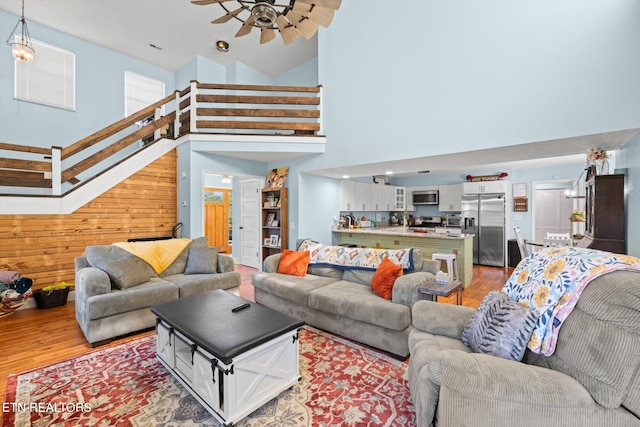 living room with wooden walls, wood-type flooring, a towering ceiling, and ceiling fan