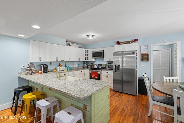 kitchen featuring light stone countertops, kitchen peninsula, stainless steel appliances, white cabinets, and dark hardwood / wood-style floors