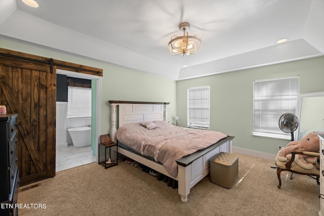 bedroom featuring connected bathroom, a barn door, light carpet, and multiple windows