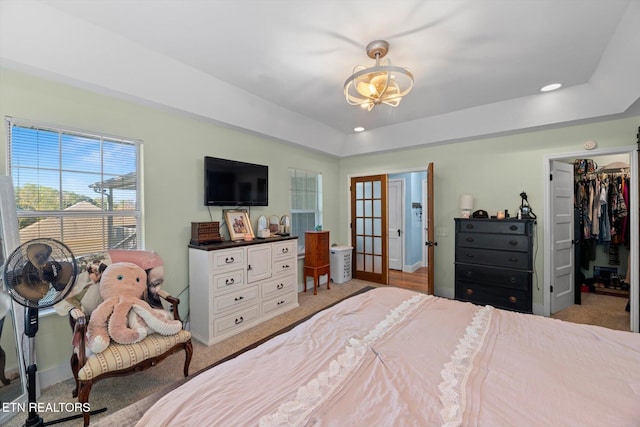 bedroom with a spacious closet, french doors, a tray ceiling, a closet, and light carpet