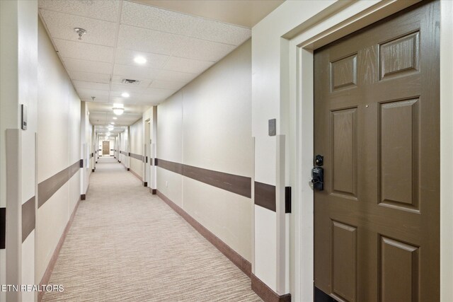 hallway featuring light carpet and a paneled ceiling