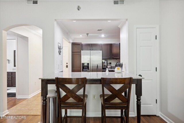 kitchen featuring light stone counters, stainless steel fridge, a kitchen breakfast bar, and light wood-type flooring