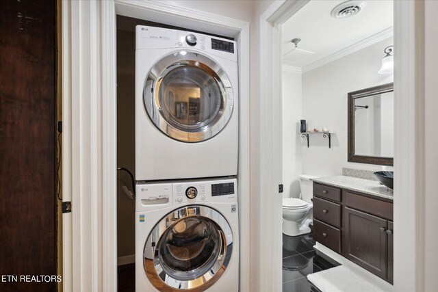 laundry area featuring crown molding, tile patterned flooring, and stacked washing maching and dryer