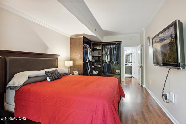 bedroom featuring connected bathroom, dark wood-type flooring, crown molding, and a closet