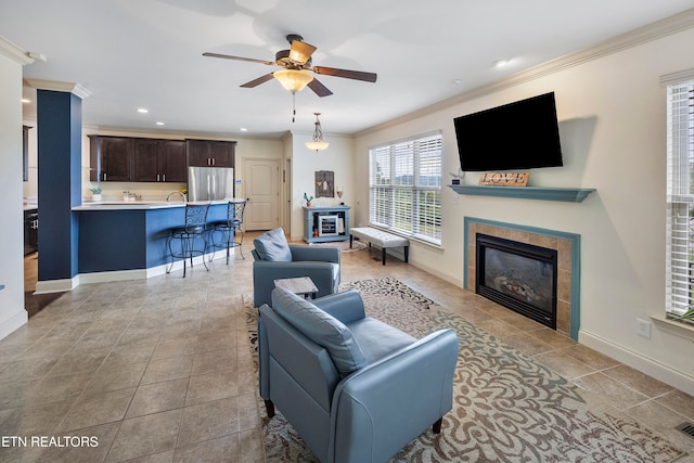 living room featuring crown molding, a tiled fireplace, and ceiling fan