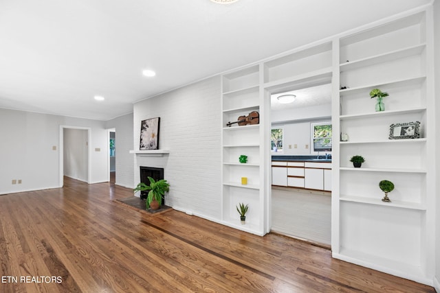 unfurnished living room with sink, a brick fireplace, and hardwood / wood-style flooring