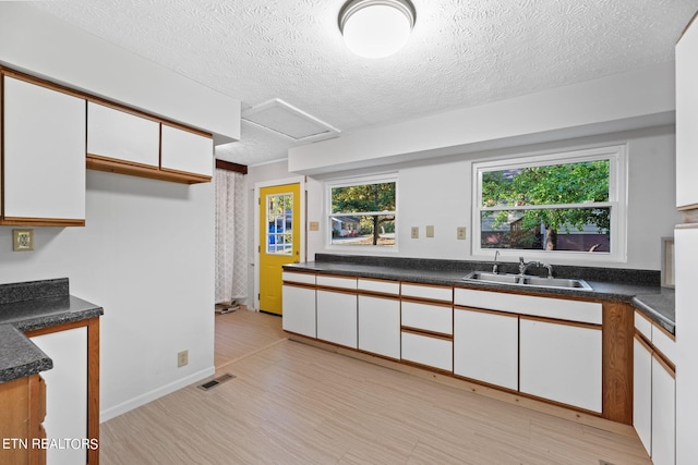 kitchen featuring sink, white cabinets, a textured ceiling, and light wood-type flooring